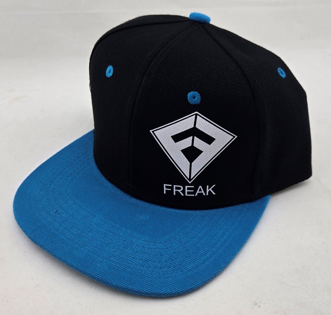 Casquette de type Snapback de couleur noire avec la visière bleue claire et le logo Freak Traction blanc - CM Surfing